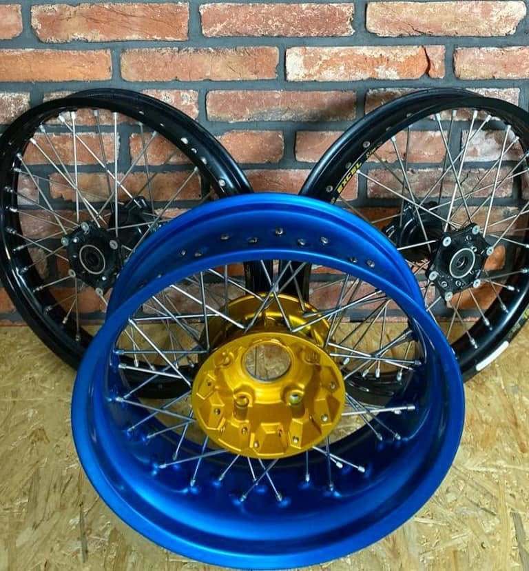 Blue rim with a gold hub and two black Excel wheels laced in our workshop